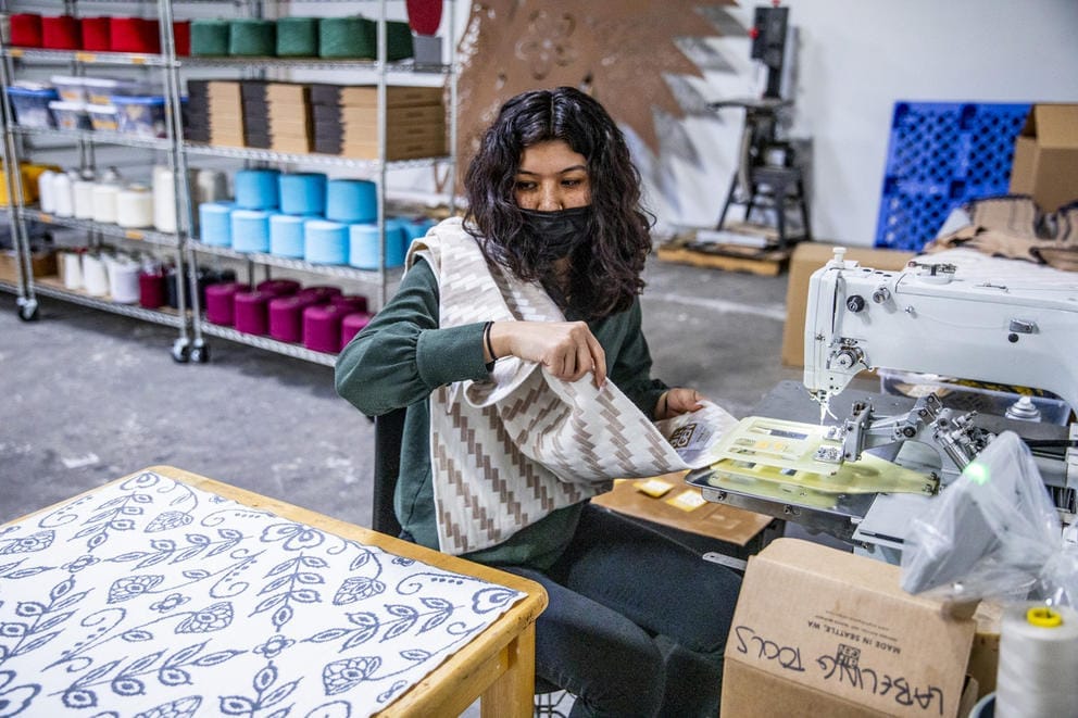 Person with mask sitting near sewing machine with blanket over shoulder