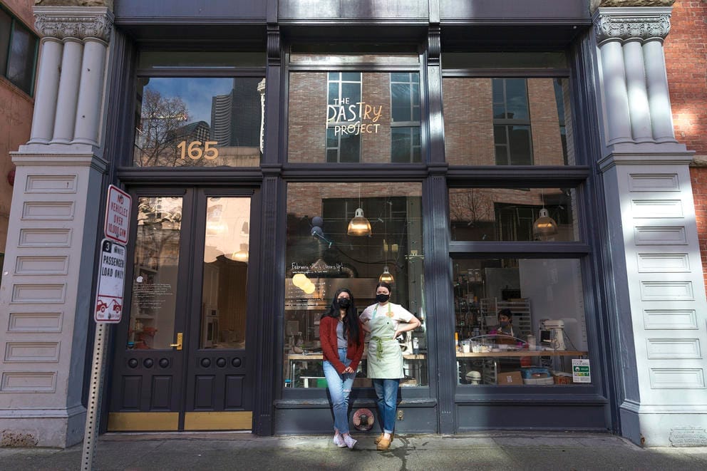 two people, masked, in front of windows of historic building
