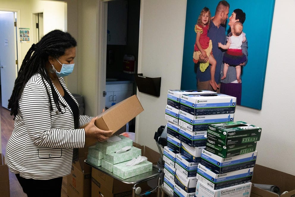 Sharon Dudash holds a box, standing in front of a other supplies that are neatly stacked
