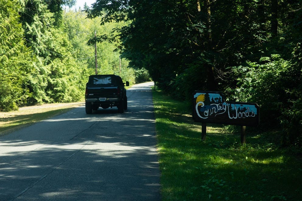 A car drives along a road surrounded by trees and a sign that says