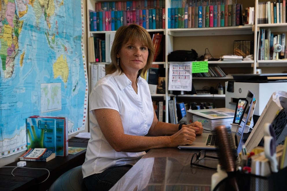 Shannon Beddo sits at a desk with books and a map of the world behind her