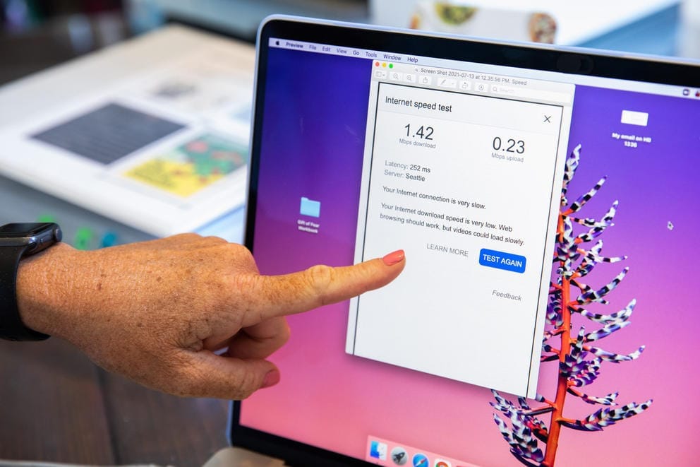 A hand points to a computer screen with an internet speed test that shows 1.42 mbps download speed and 0.23 mbps upload speed
