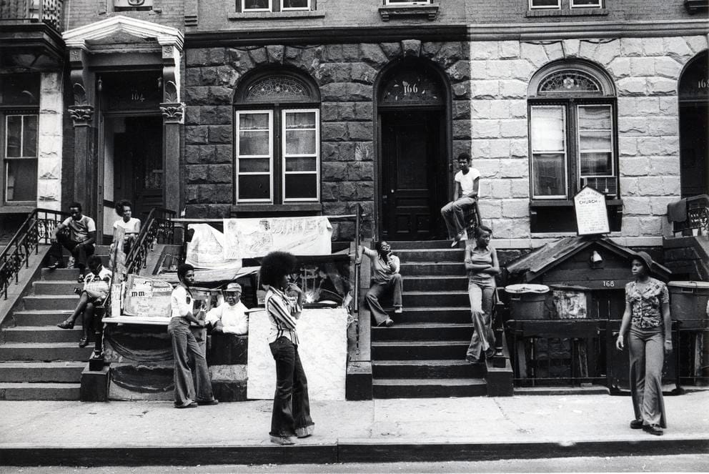 Black and white photo of a street in Harlem with a variety of people walking and sitting