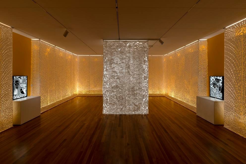 A pillar of paper scrolls cut with symbols in a room clad with intricately cut paper, glowing with a backlit goldon glow