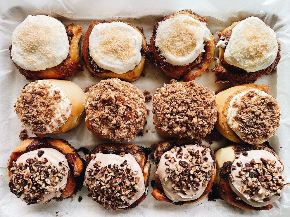 three rows of four cinnamon rolls topped with icing and crumble
