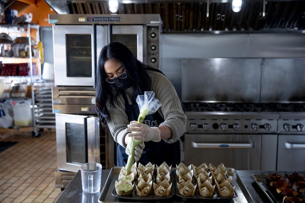 Person in professional kitchen piping icing on small cakes wrapped in paper