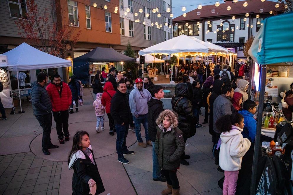 People walk around outside in a courtyard where lights hang from above and tents are set up