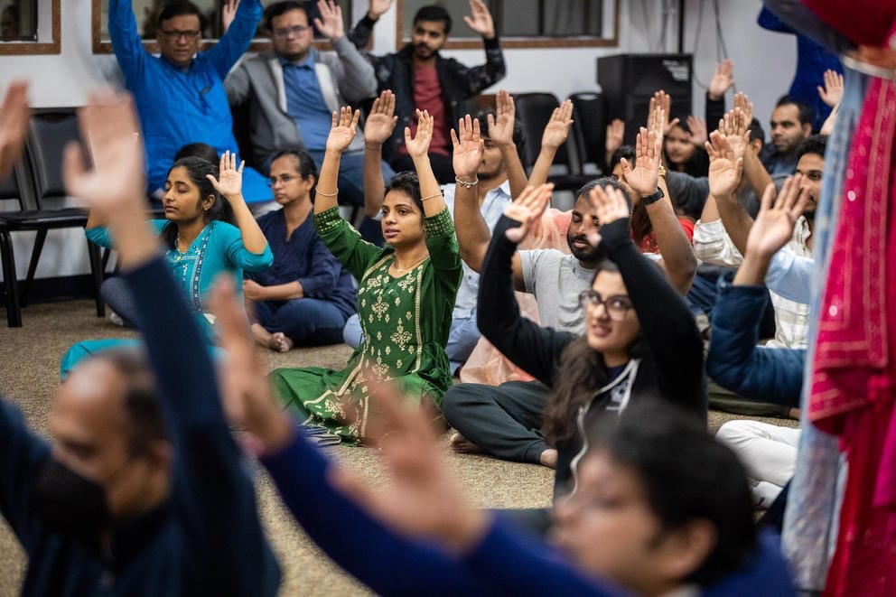A room full of seated people with their hands raised