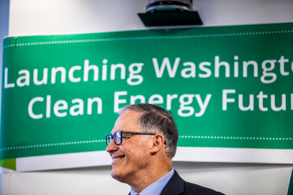 Inslee standing in front of a banner reading