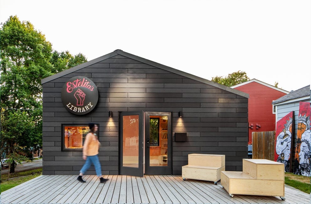 wooden, dark structure with patio out front and person walking by