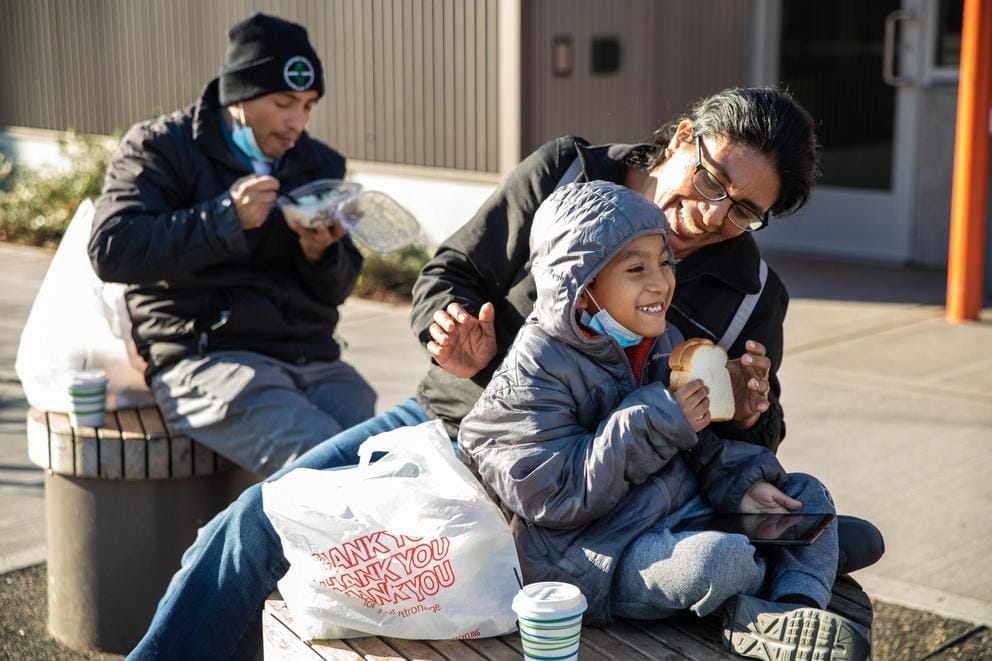 a man, woman, and little boy eat a meal outside in the sun