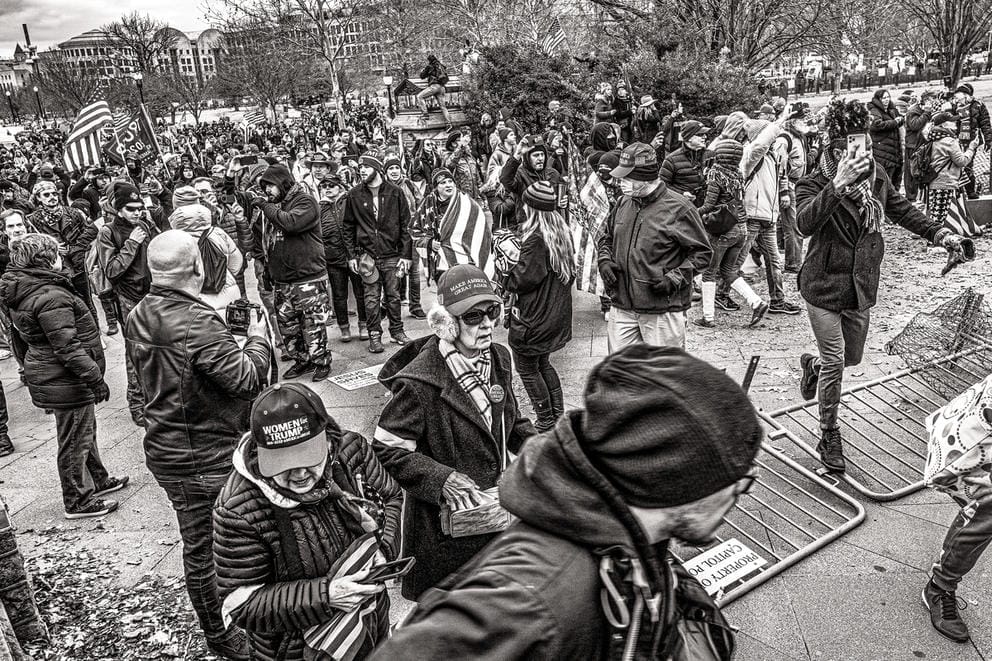 People walk over a fence, one woman wearing earmuffs, another a shopping bag, in a black and white photo