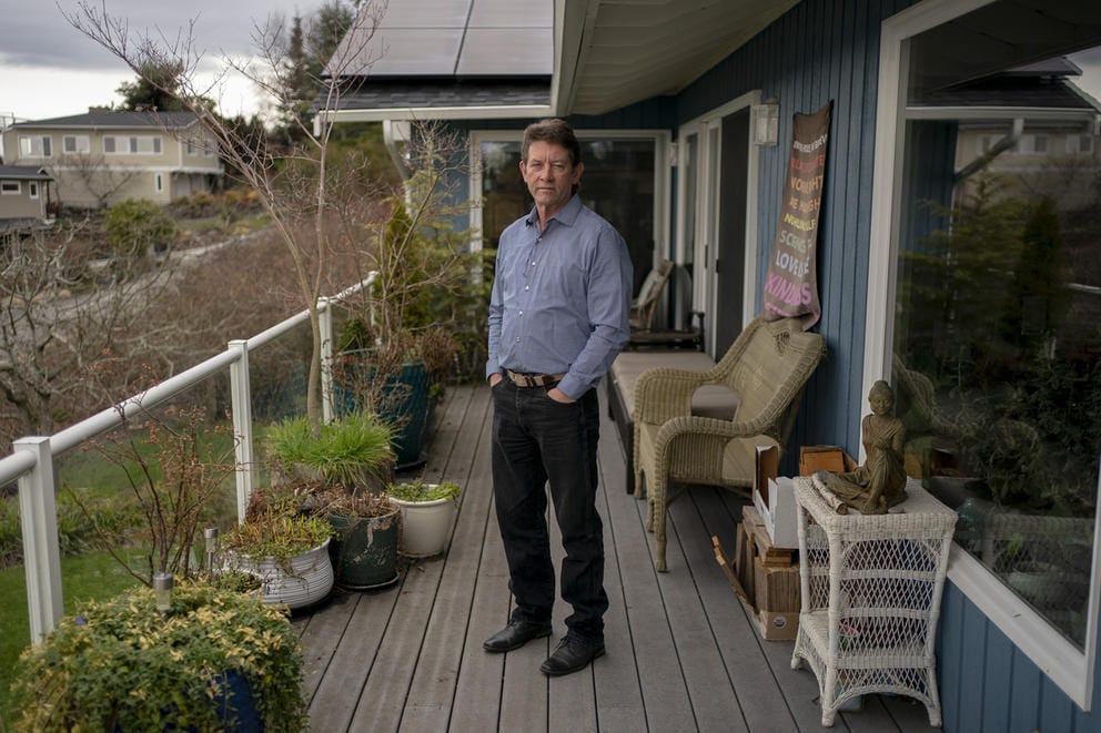 A man in a light blue shirt and dark pants stands on a balcony