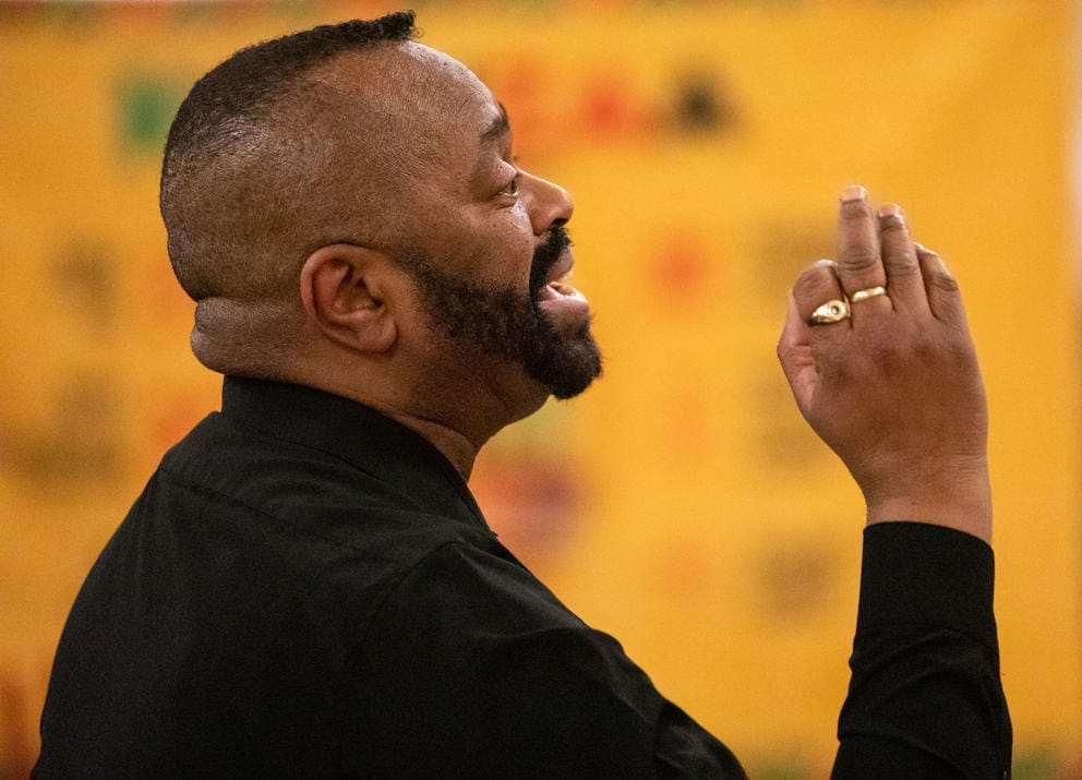 A close up of a man with his hand up conducting a choir