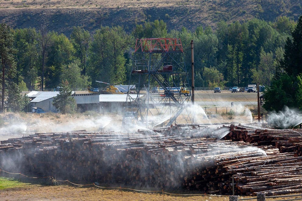 Logs are piled near a tower and helicopter