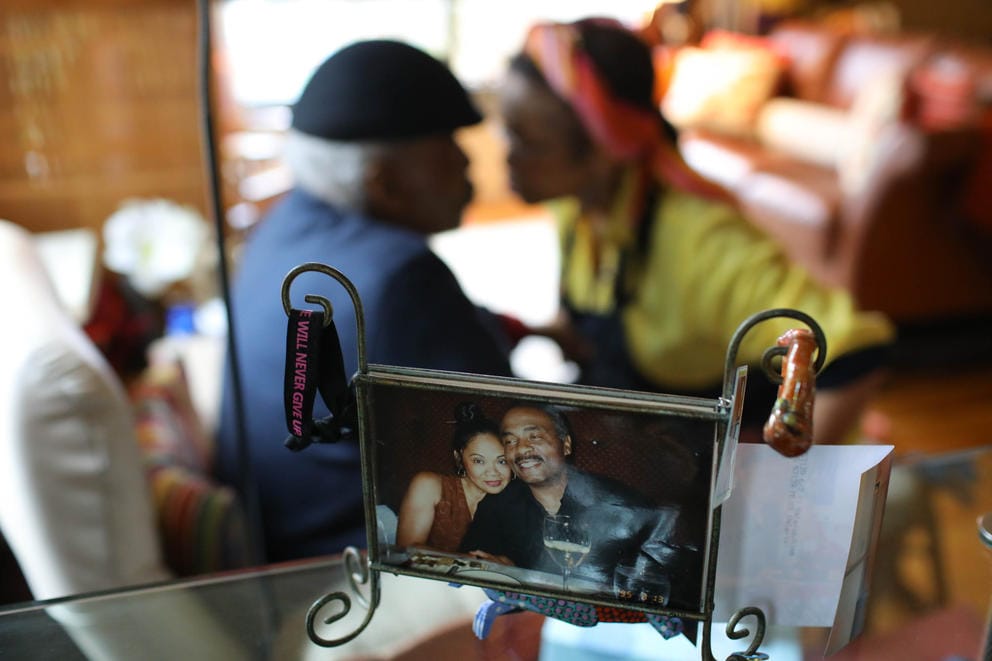 A photograph of a couple sits on a shelf, the same couple is seen out of focus in the room behind the picture frame.