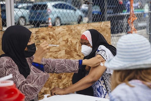 A health worker injects a vaccine into a female patient's arm at an outdoor clinic