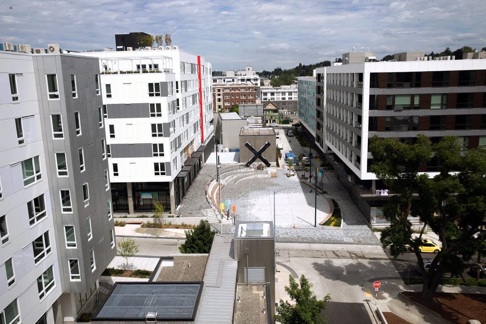 large buildings surrounding a round, gray plaza with large X shaped artwork at the end