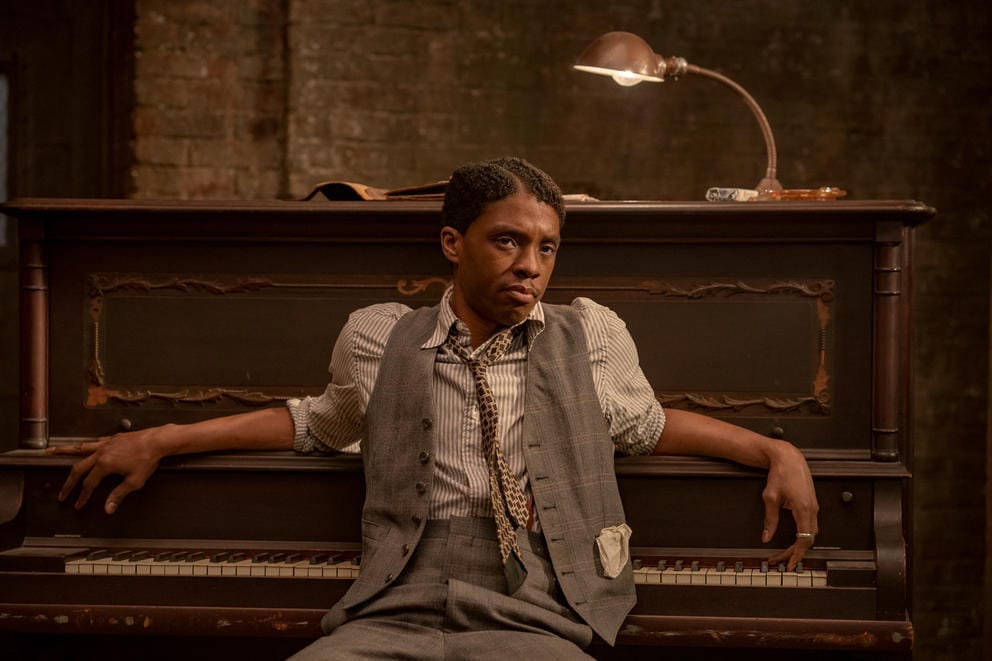 Actor in jazz era clothes sitting in front of piano.