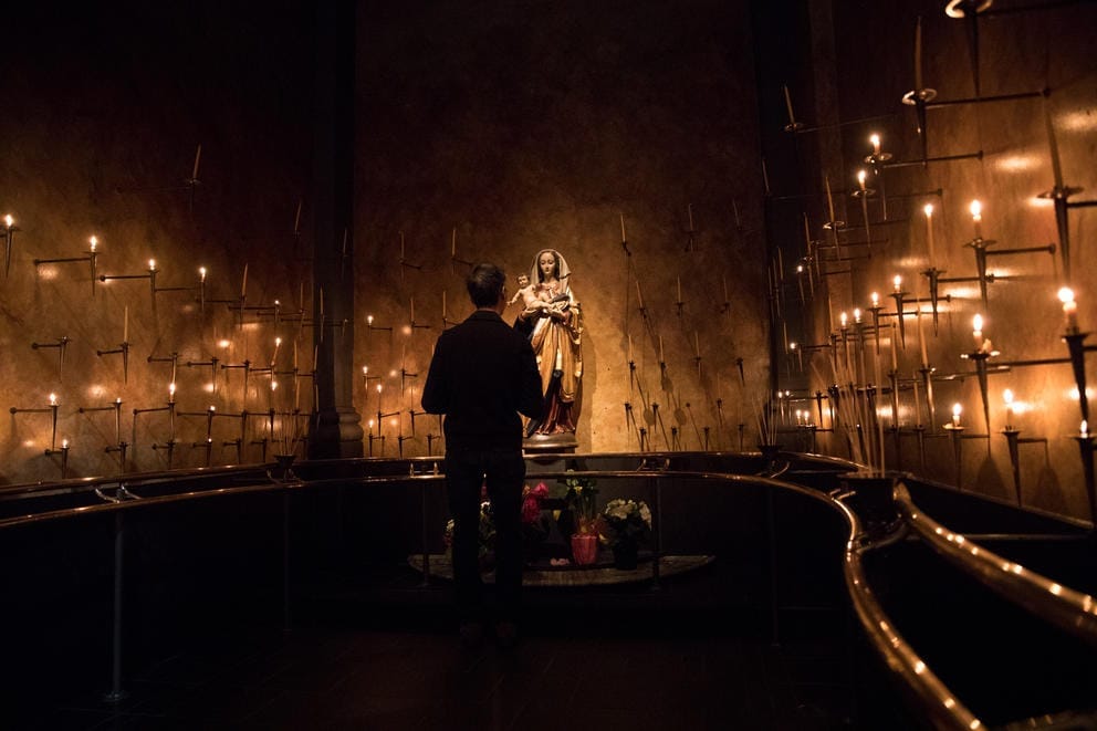 A parishioner stands inside a candlelit altar with Virgin Mary and Jesus during a public veneration at St. James Cathedral in Seattle.