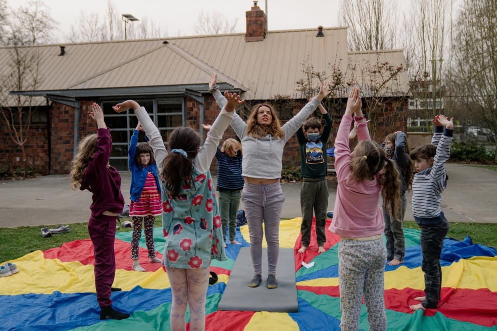 A teacher leads students in a yoga exercise outside.