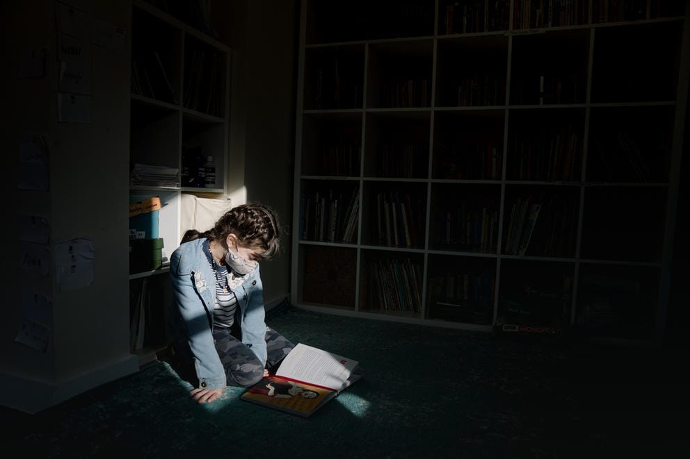 A young student sits on a floor and reads.
