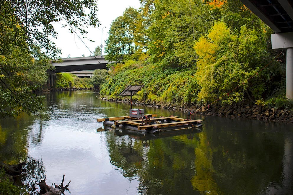 A research barge floats in a river under a bridge.