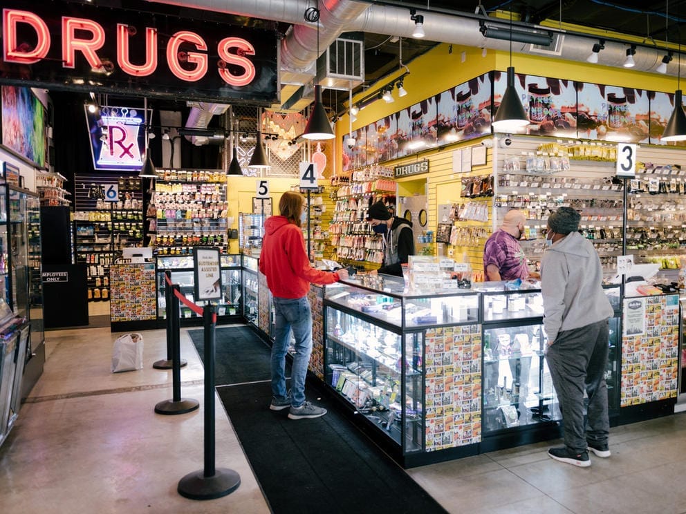 Customers approach a display case filled with marijuana products. At left in the background a sign reads
