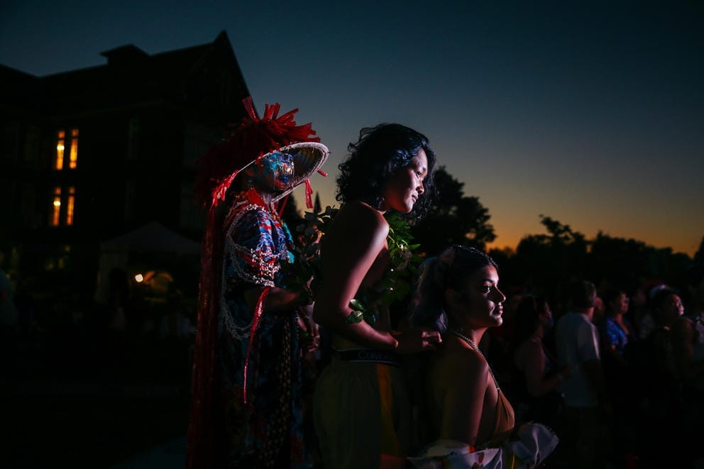 A faint orange glow lights the evening sky as three figures stand together in a sliver of light