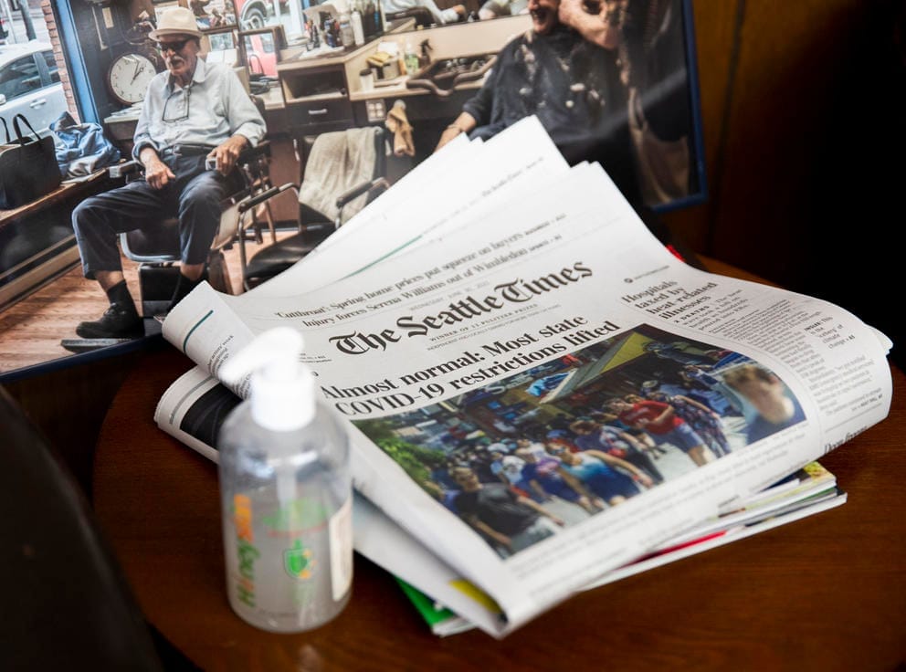 A copy of the Seattle Times newspaper rests on a table next to a bottle of hand sanitizer. The headline read