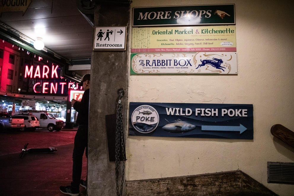 man stands near a wall that has a variety of signs on it, including one saying