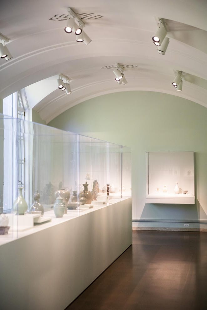 A domed, long room with a long glass display case featuring colorful pottery arranged by color. Light enters the room from the left.