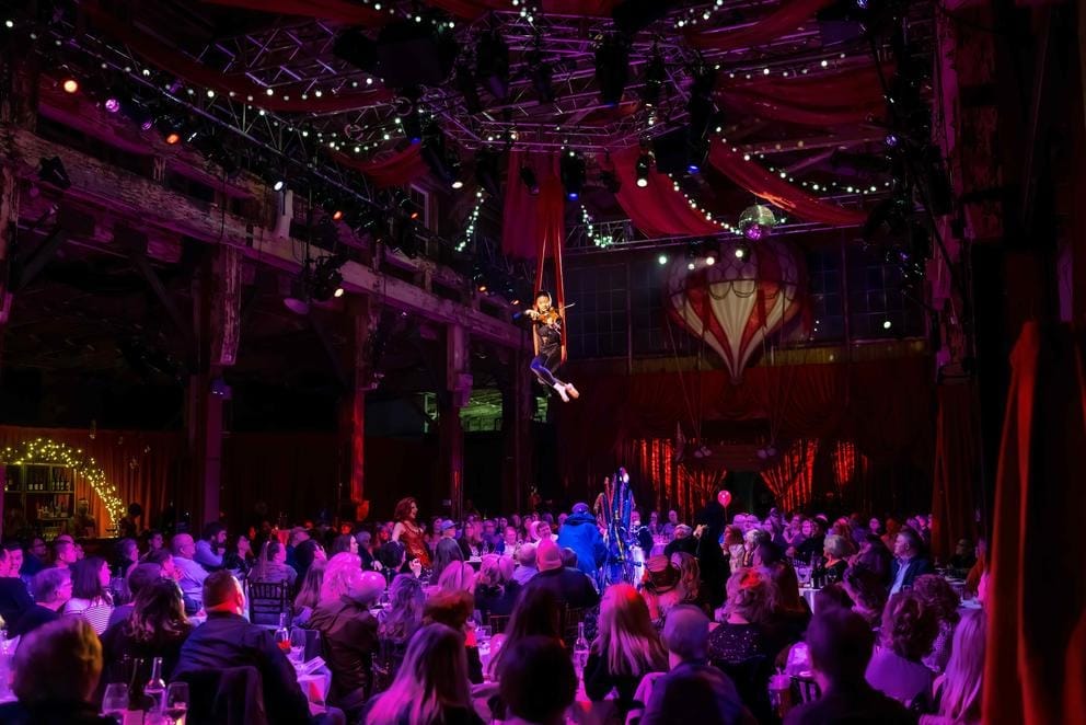 Person performs on violin while suspended high in the sky, an audience below her