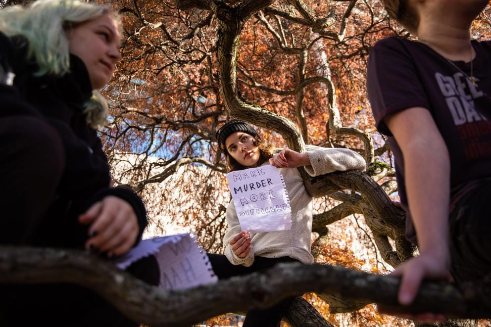 A student leaning against a tree holds a sign saying