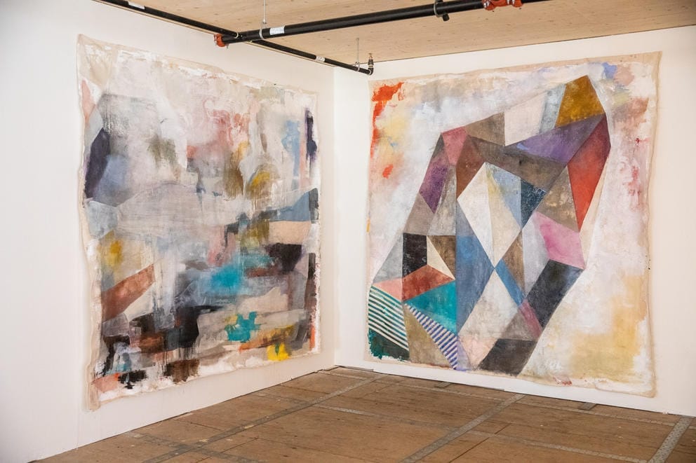 Two large pieces of abstract art hang in a corner