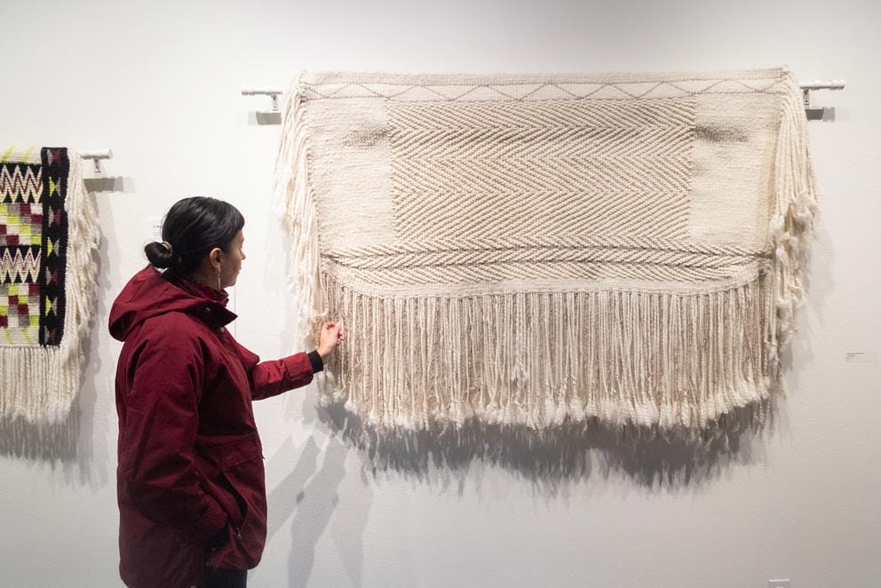 Person in red coat stands near white blanket with fringes and points to it