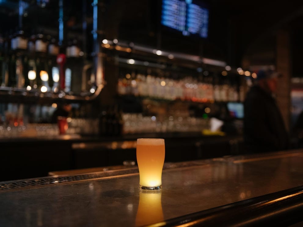 An illuminated beer sits on an empty bar