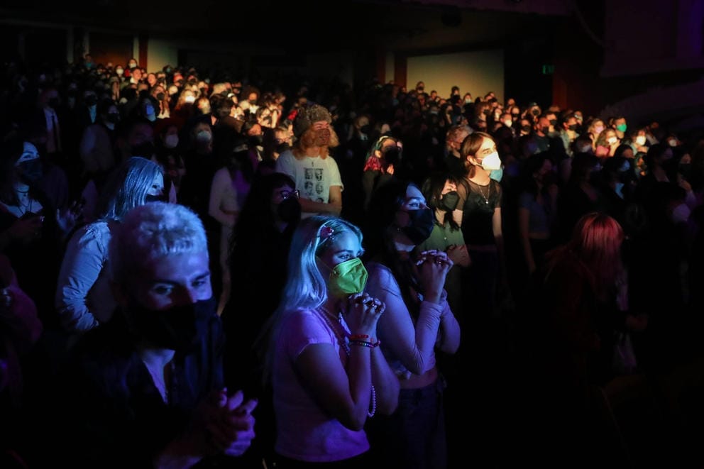 Person in facemask bathing in blue light amid larger crowd
