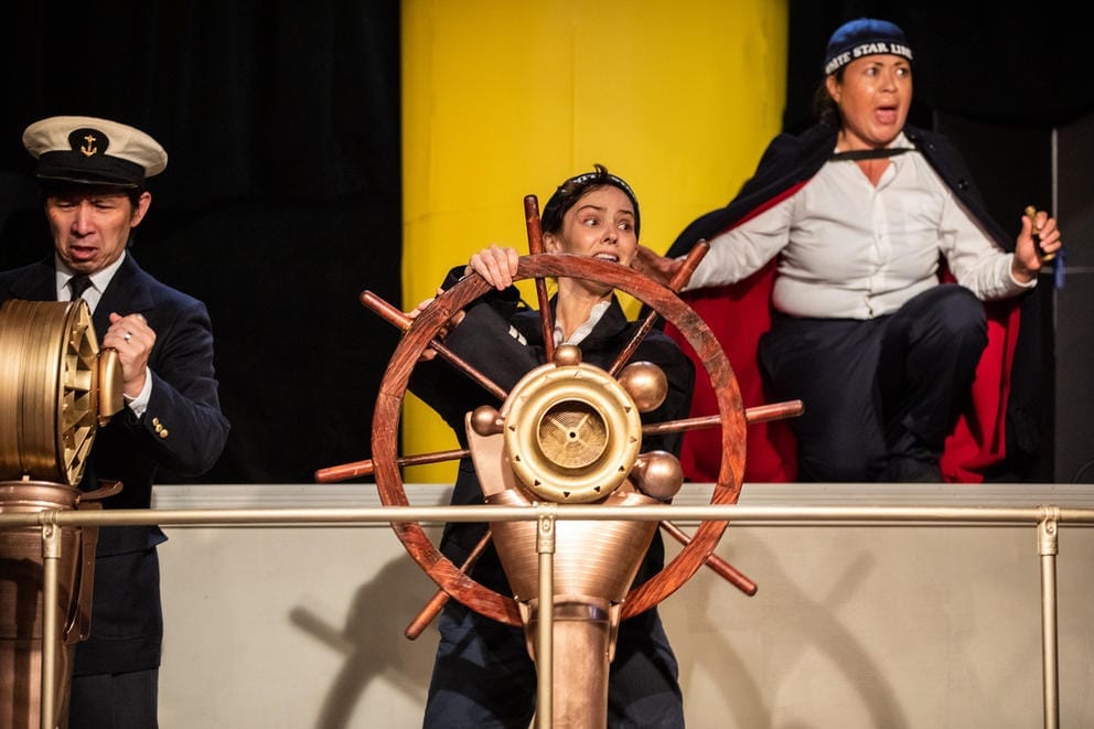 Person on stage playing a captain, standing behind a helm