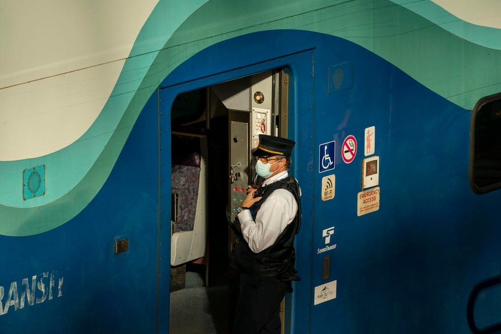 a comuter rail conductor stands outside of a blue, green, and white sounder train in Seattle