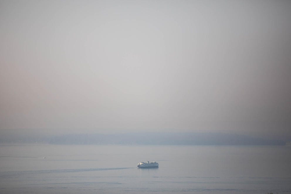 A ferry wades through wildfire smoke in the foreground of mountains