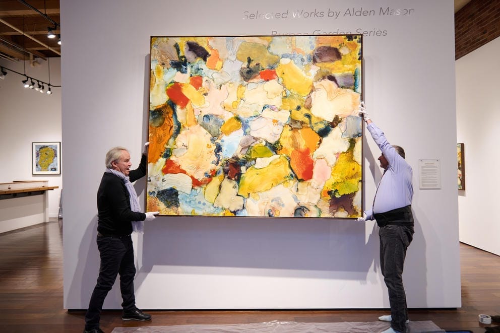 Two people take a bright painting off the wall