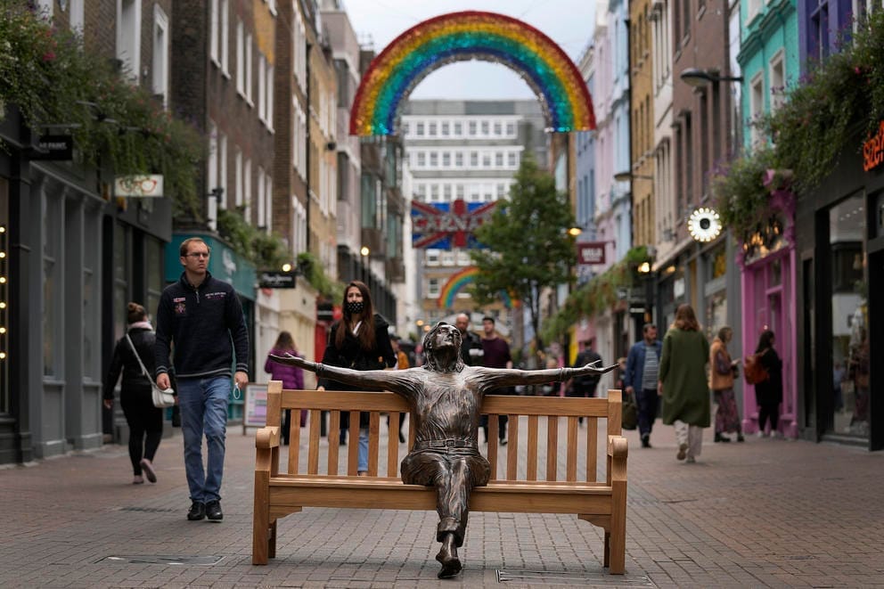 a busy plaza in london with people walking around a bronze statute of john lennon