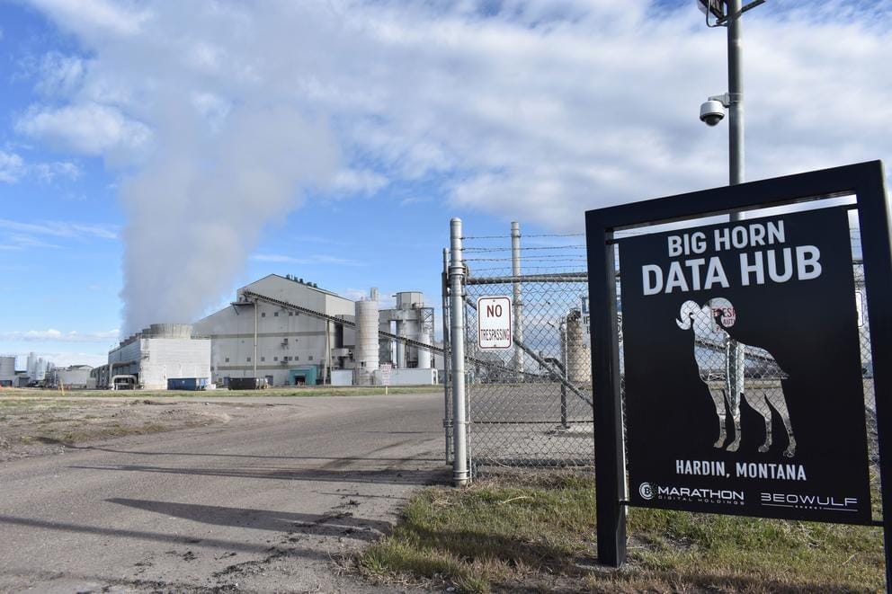 A coal-fired power plant blows smoke behind a sign of the cryptocurrency