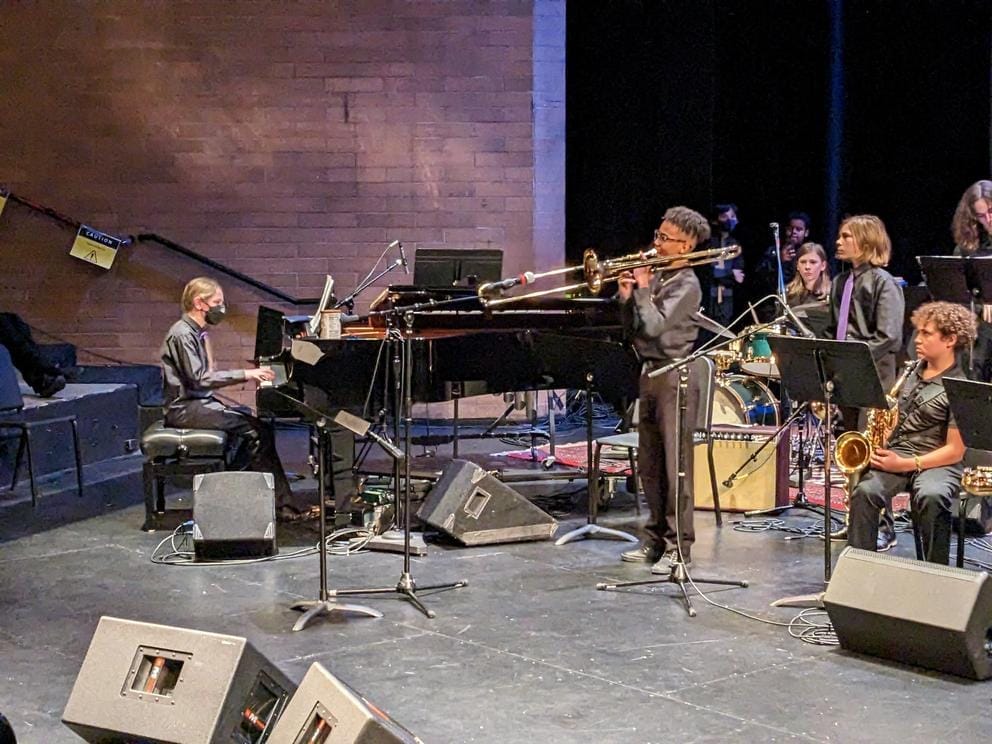 A boy plays the trombone while another plays the piano on a stage