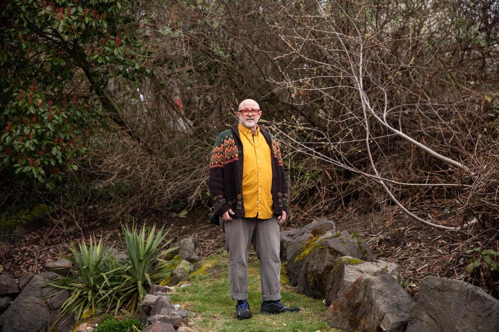Roger Kelley stands in an overgrown lot surrounded by branches and vines