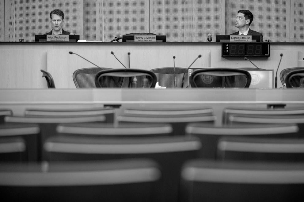 two seattle city councilmembers sit behind desks in seattle city council chambers