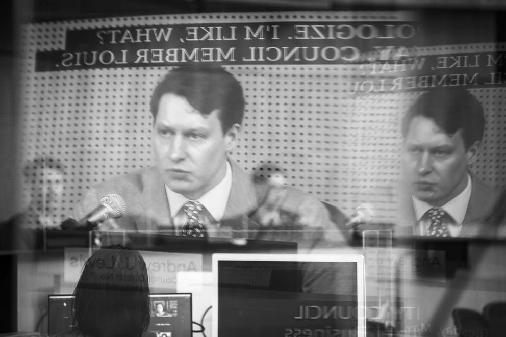 councilmember andrew lewis's face reflected in plexiglass at city hall