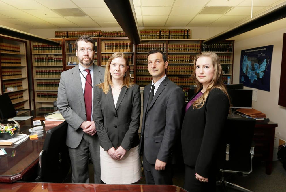Four attorneys stand shoulder to shoulder in their legal office.