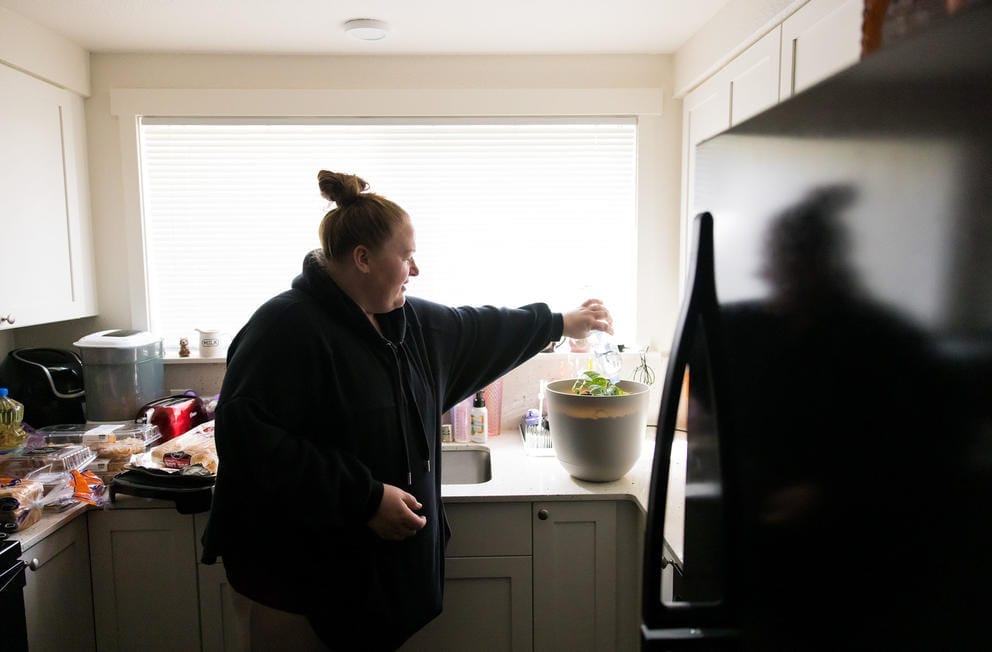 Heather Nguyen waters her plant with bottled water in her home on the Joint Base Lewis-McChord base